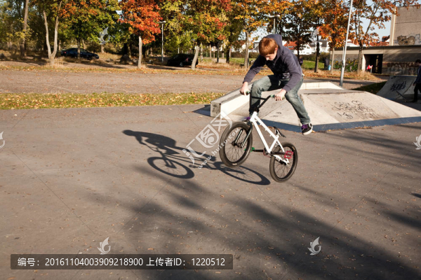 年輕的紅頭發(fā)的男孩是他的自行車在玩滑板公園跳