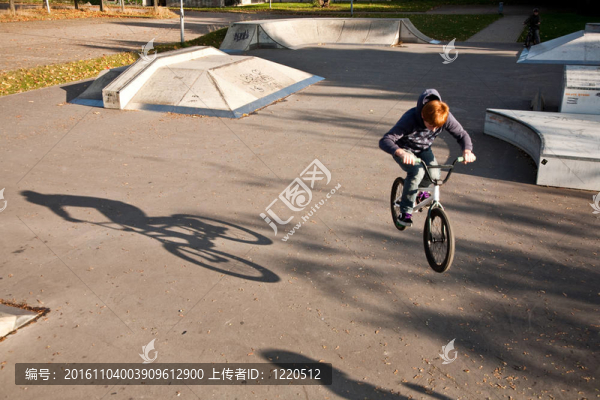 年輕的紅頭發(fā)的男孩是他的自行車在玩滑板公園跳