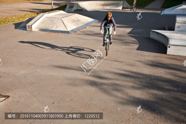 年輕的紅頭發(fā)的男孩是他的自行車在玩滑板公園跳