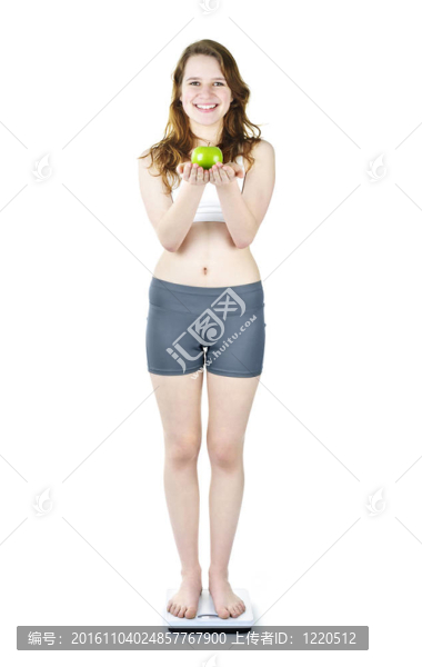 年輕的微笑女孩在浴室秤持有蘋果