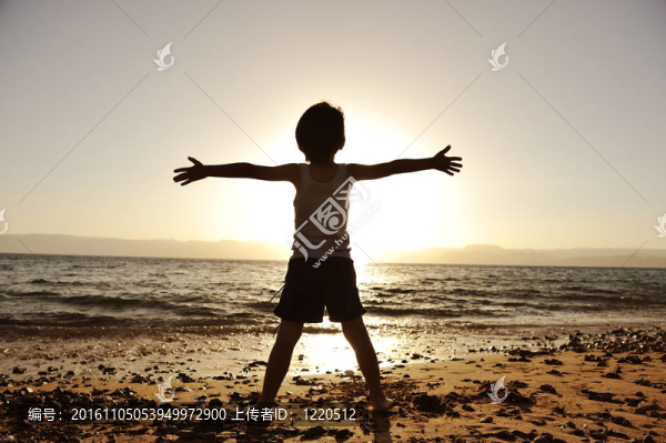 孩子在海灘上的輪廓；舉起他的手；向著太陽