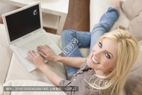 年輕的金發(fā)女人在家里用筆記本電腦在沙發(fā)上