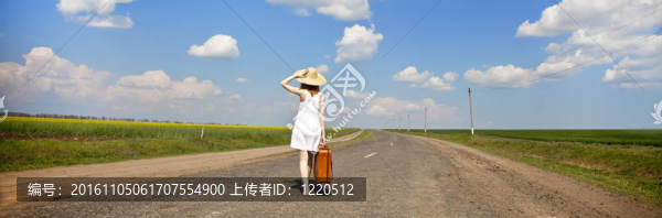 鄉(xiāng)村路上帶著手提箱的寂寞女孩。全景照片。