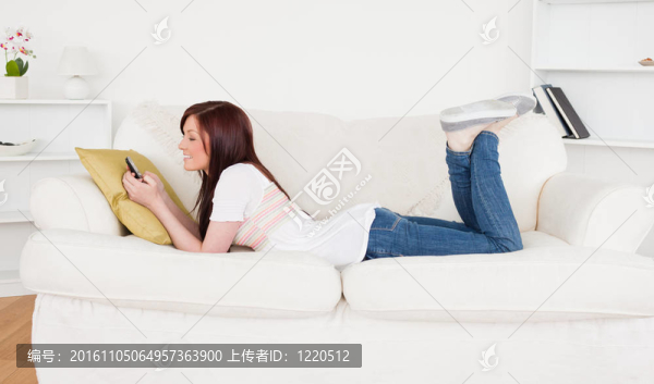 漂亮的紅發(fā)女性在客廳的沙發(fā)上躺在手機(jī)上寫(xiě)著短信