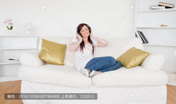 漂亮的紅發(fā)女性一邊坐在客廳的沙發(fā)上一邊聽音樂一邊戴著耳機