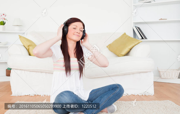 美麗的紅發(fā)女性聽音樂與耳機(jī)，而坐在地毯在客廳