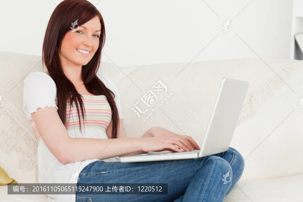 漂亮的紅發(fā)女人坐在客廳的沙發(fā)上放松自己的筆記本電腦