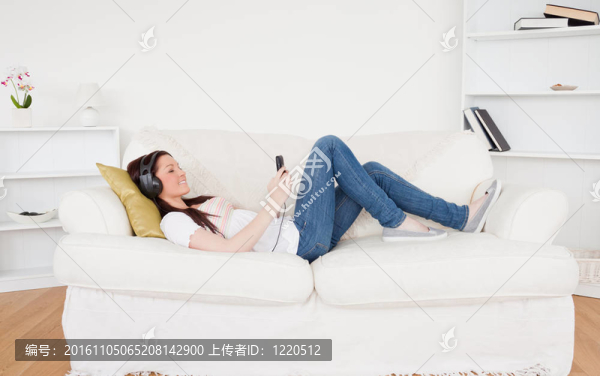 迷人的紅發(fā)女性用耳機聽音樂，同時躺在客廳的沙發(fā)上