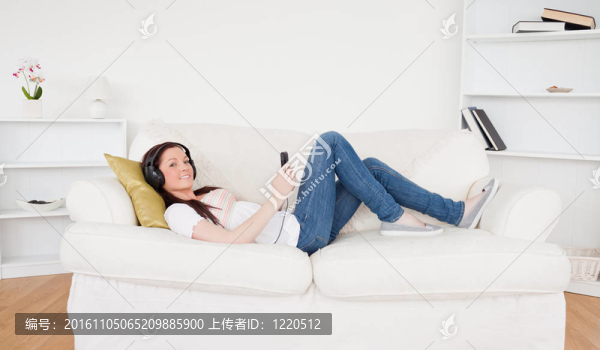 美麗的紅發(fā)女性用耳機聽音樂，同時躺在客廳的沙發(fā)上