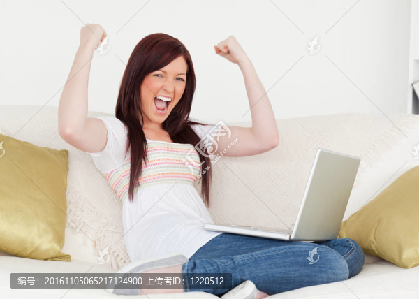 迷人的紅發(fā)女子在客廳里的沙發(fā)上坐著筆記本電腦后，高興地賭博