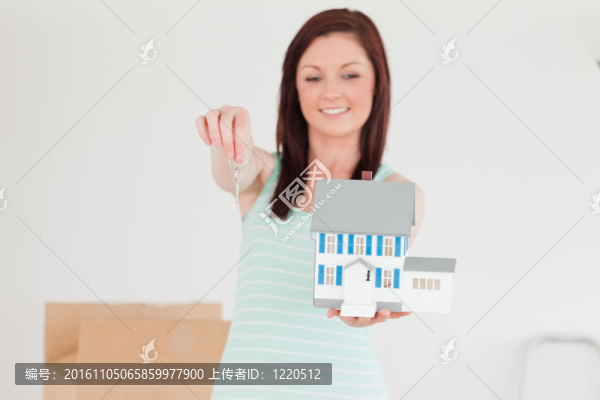 漂亮的紅發(fā)女人站著拿著一個(gè)小房子