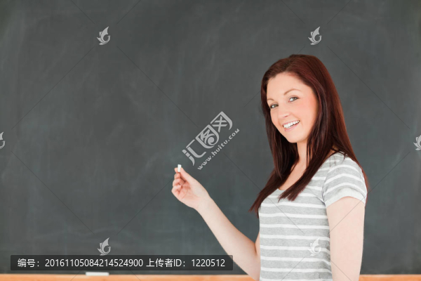 面帶微笑的年輕女子站在黑板前用粉筆在教室里