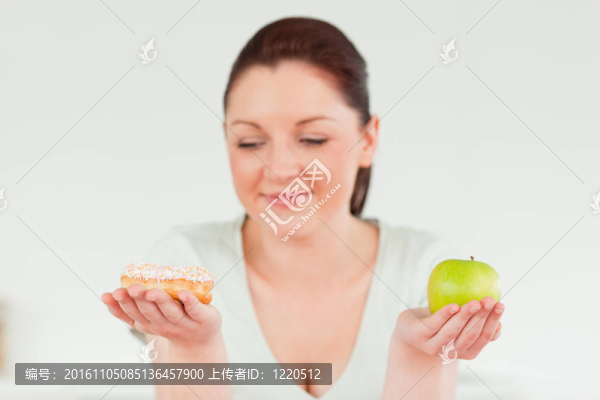 有吸引力的女人冒充一邊拿著面包圈和一個綠蘋果