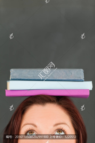 快樂(lè)的年輕婦女戴著書(shū)在她的頭與相機(jī)集中在她的頭在教室里
