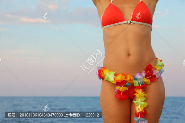 美麗的年輕女子穿著泳裝站在海灘上。在腰部的花夏威夷花環(huán)