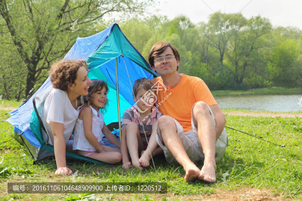 幸福的家庭-母親；父親；小女孩和小男孩；坐在藍(lán)色帳篷里，在陽光河上的綠色草坪上歡笑