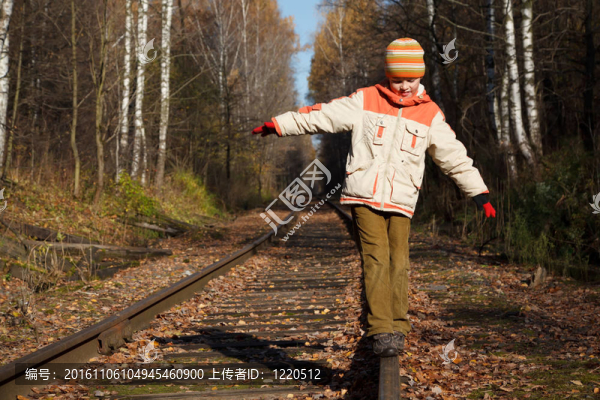 陽光明媚的一天，男孩沿著鐵路走。他穿著一件夾克和帽子。