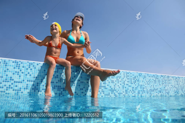 母親和女兒坐在欄桿的游泳池和欣然抬起他