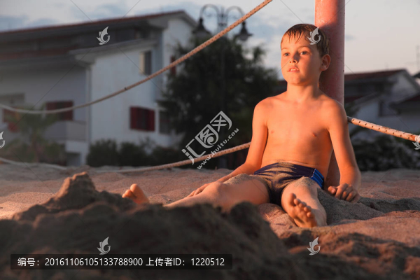 憂郁的男孩洗完澡，坐在海灘上的沙子在晚上