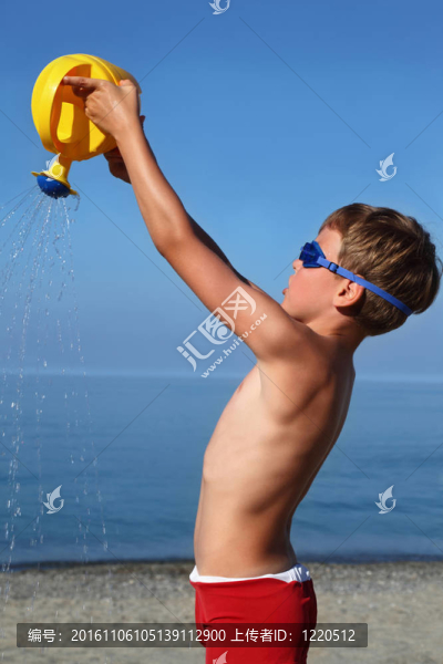 男孩站在海灘上，白天和沙子澆水澆水