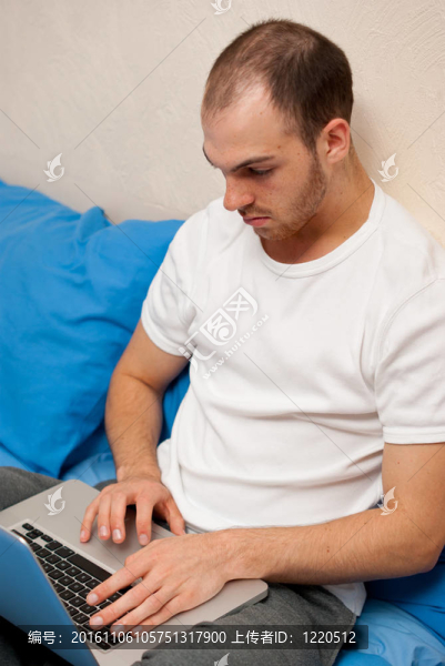 英俊的男人在床上使用筆記本電腦
