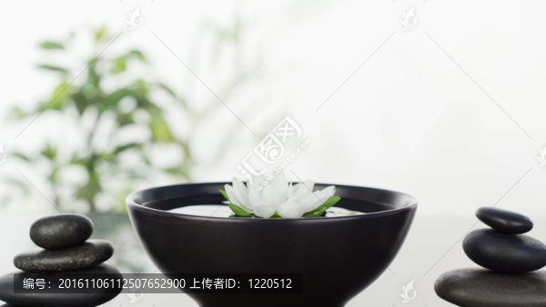 白色的花漂浮在碗中間和兩邊的兩個(gè)黑色卵石堆疊