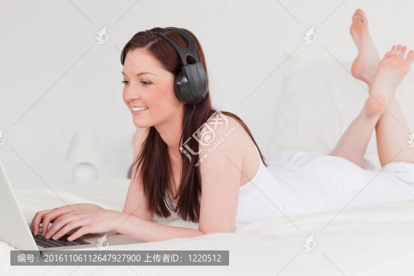 漂亮的紅發(fā)女性用她的筆記本電腦和耳機放松，躺在床上