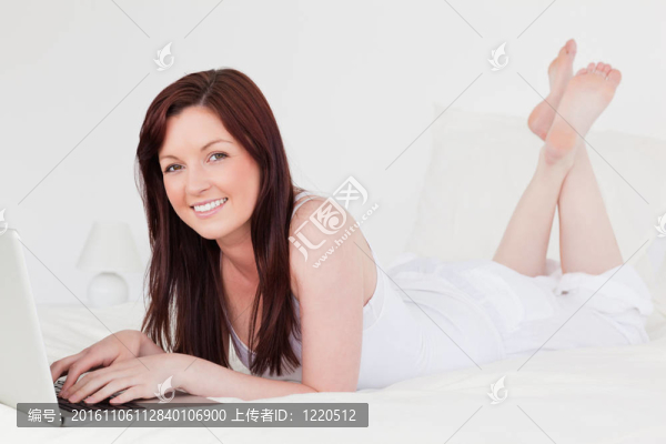 美麗的紅發(fā)女性放松與她的筆記本電腦，而躺在她的床上