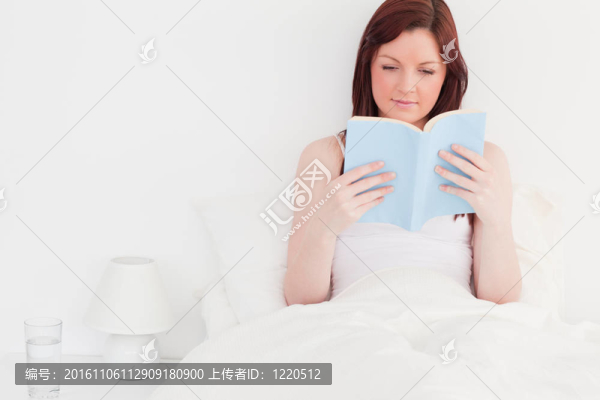 迷人的紅發(fā)女人坐在床上看書(shū)