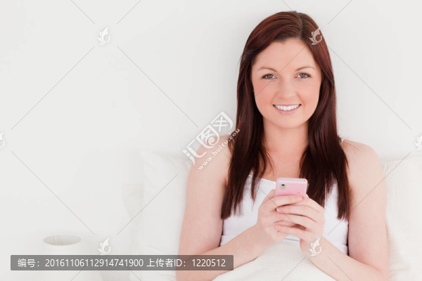 漂亮的紅發(fā)女人坐在床上寫手機(jī)上的文字