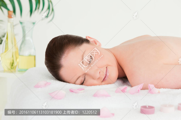美麗的女人躺在按摩桌上點(diǎn)燃的蠟燭，與花瓣