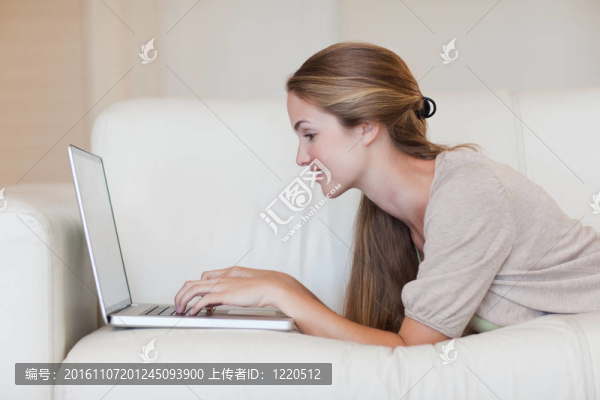 側(cè)面的女人躺在沙發(fā)上與她的筆記本電腦