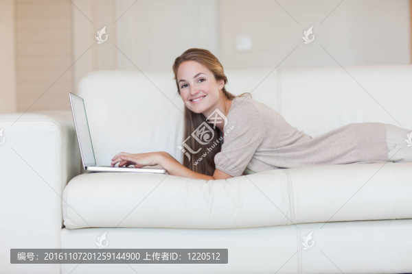 側(cè)面的女人躺在沙發(fā)上與她的筆記本電腦