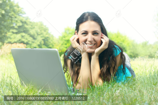 美麗的年輕女子在公園使用筆記本電腦的肖像
