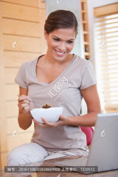 女人一邊看著筆記本一邊吃著麥片
