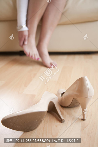 年輕女子在脫下高跟鞋后，坐在家里揉著腳.