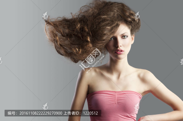 年輕漂亮的頭發(fā)卷曲的頭發(fā)飛揚(yáng)的創(chuàng)意發(fā)型美容時(shí)尚寫真。她看著鏡頭，把頭發(fā)舉在左、右手放在左髖上.。
