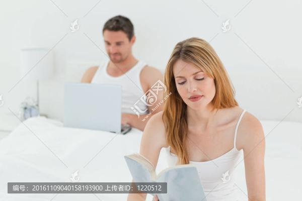 男人在他的筆記本電腦上，而他的妻子在看書