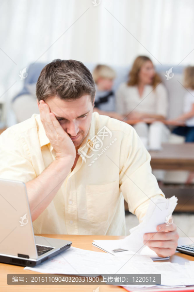男人計(jì)算他的賬單，而他的家人在沙發(fā)上
