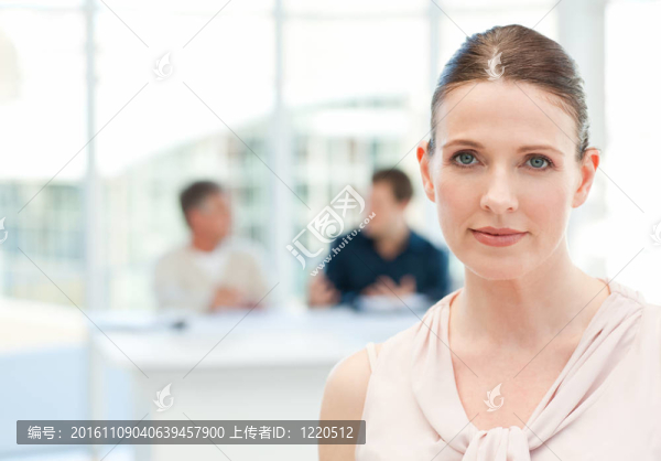 嚴(yán)重的商人看著鏡頭，她的同事在辦公室聊天