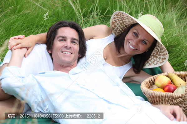 夫妻倆躺在草地上，拿著一籃水果