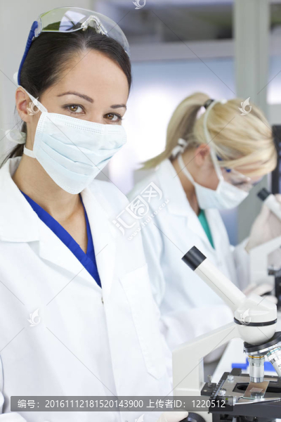 一個(gè)女性醫(yī)學(xué)或科學(xué)研究人員或醫(yī)生用顯微鏡在實(shí)驗(yàn)室與她的同事在她身后的焦點(diǎn)。