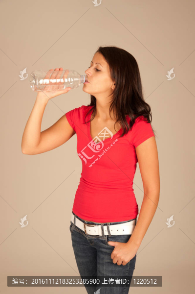 迷人的年輕女子穿著紅色T恤和牛仔褲喝瓶裝水