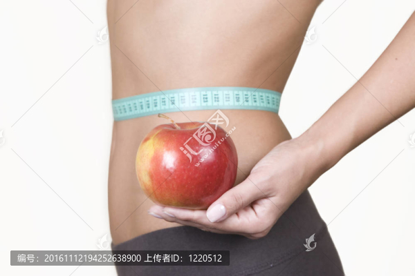 女人一邊拿著紅蘋果一邊測量她的腰