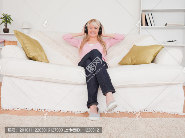 美麗的金發(fā)女性聽音樂的耳機，而坐在客廳的沙發(fā)上