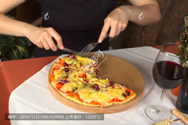 女人在一杯紅酒站在比薩店吃素食比薩（選擇性焦點(diǎn)；焦點(diǎn)在手；餐具及餐具的披薩）
