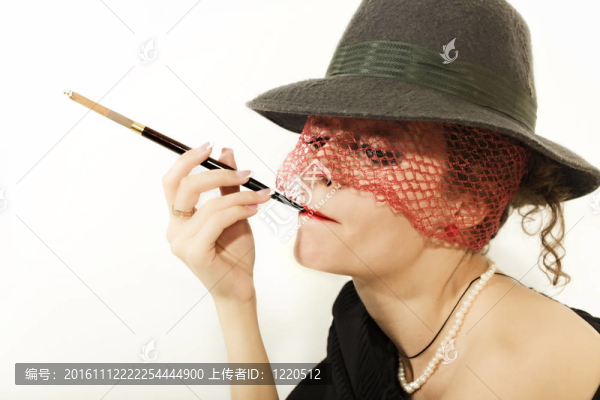 年輕的美麗女人與香煙在帽子與面紗孤立在光的背景