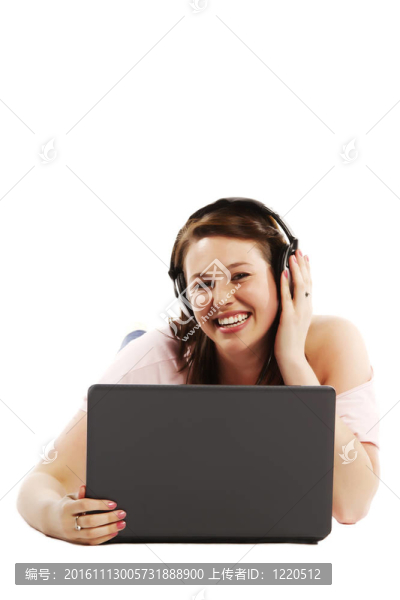 快樂的年輕女子躺在地板上聽音樂在她的筆記本電腦在白色背景