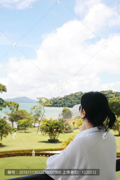 美麗的女士在陽臺(tái)上喝咖啡，擁有美麗的花園和海灘景觀
