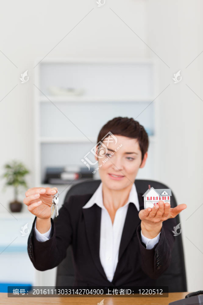 一個女人展示一個微型房子和鑰匙的肖像